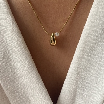 Colar dourado com pendente e pérola em pescoço, roupa branca