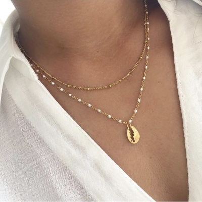 Colar duplo dourado com pérolas e medalha com desenho de folha, usado com camisa branca