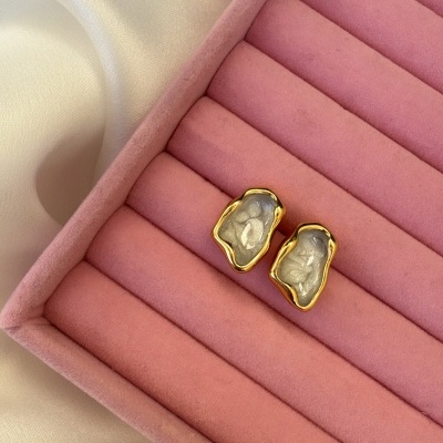 Brincos dourados com centro prateado em caixa rosa de veludo numa superfície branca acetinada.