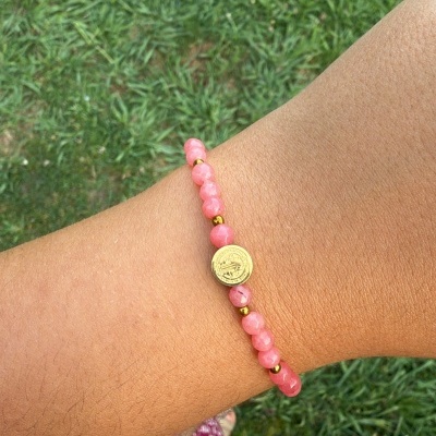 Pulseira rosa e dourada com moeda central no pulso