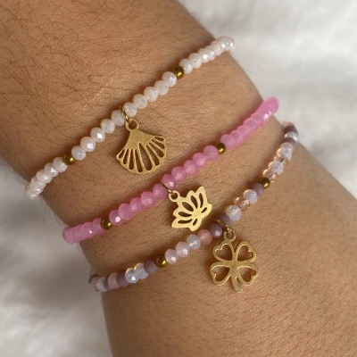 Três pulseiras rosa com pendentes dourados no pulso