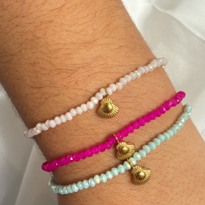 Pulseiras coloridas com pendente dourado em forma de concha no pulso