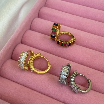 Três pares de brincos em aro com pedras coloridas e transparentes numa caixa rosa acolchoada.