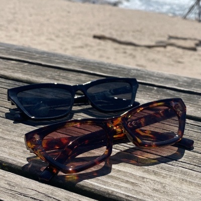 Dois pares de óculos de sol numa mesa de madeira com vista para a praia e mar.