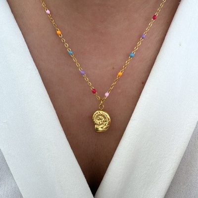 Colar dourado com contas coloridas e pendente abstrato usado sobre camisa branca