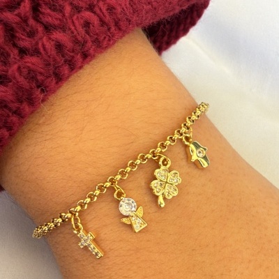 Pulseira dourada com pendentes diversos em pulso com camisola vermelha de malha