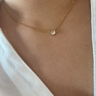 Colar dourado com pendente redondo pequeno usado no pescoço com camisa branca