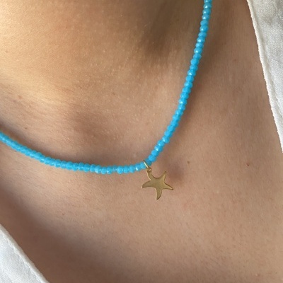 Colar azul com pendente estrela do mar dourado num pescoço.