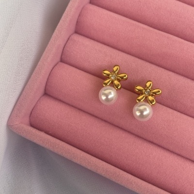 Brincos dourados em forma de flor com pérola numa caixa de veludo rosa