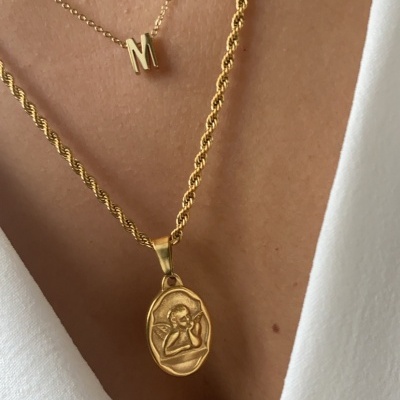 Colares dourados com pendente oval e letra M sobre pele e camisa branca