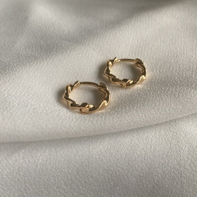 Brincos de argola dourados com design torcido sobre tecido branco.