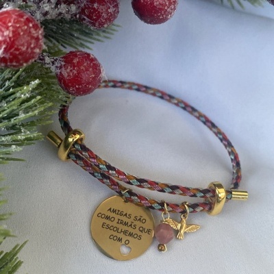Pulseira trançada com medalhão dourado e pendentes, junto a decoração de Natal com bagas vermelhas.