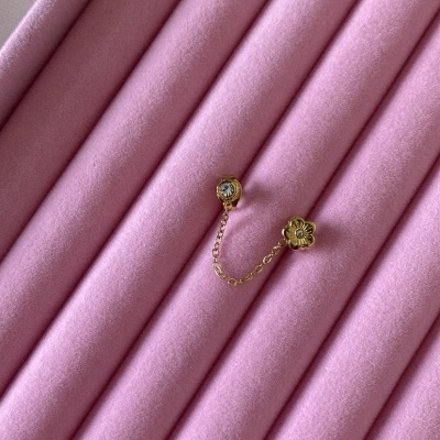 Brinco dourado com corrente e decoração floral sobre veludo rosa acolchoado