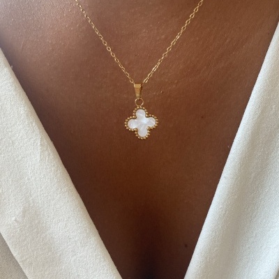 Colar dourado com pendente em forma de trevo e parede branca