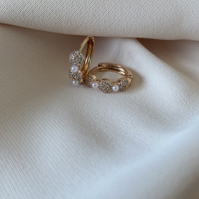 Brincos dourados com pérolas e pedras brilhantes sobre tecido branco