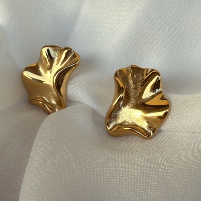 Brincos dourados com forma irregular sobre tecido branco