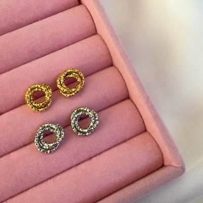 Quatro brincos circulares dourados e prateados em caixa rosa de veludo sobre tecido branco