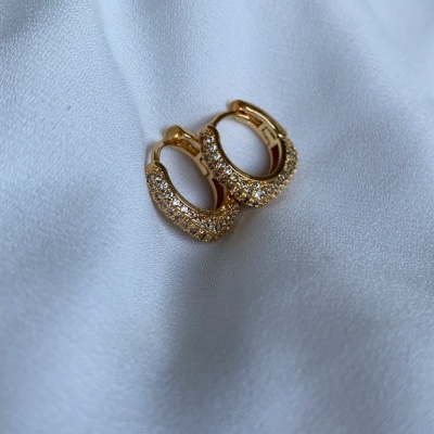 Brincos dourados em forma de argola com pedras brilhantes sobre tecido branco