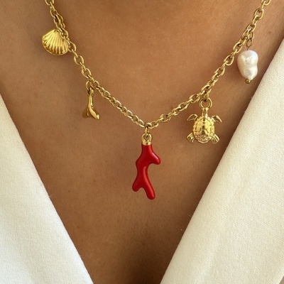 Colar dourado com pendentes marinhos e pérola sobre pele e roupa branca