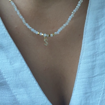 Colar com contas brancas e douradas e pendente em forma de S, usado com camisa branca.