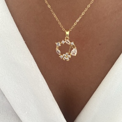 Colar dourado com pendente circular decorado com pedras, usado sobre pele e blusa branca