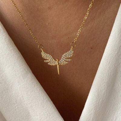 Colar dourado com pendente de asas brilhantes em pele clara e vestido branco.