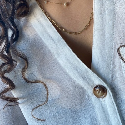 Colares dourados com pérolas e elos em pescoço com camisa branca e botões castanhos