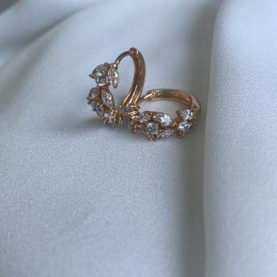 Brincos dourados com pedras transparentes sobre tecido branco