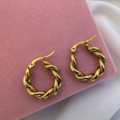 Brincos de argola torcidos metálicos dourados sobre fundo rosa aveludado e branco.