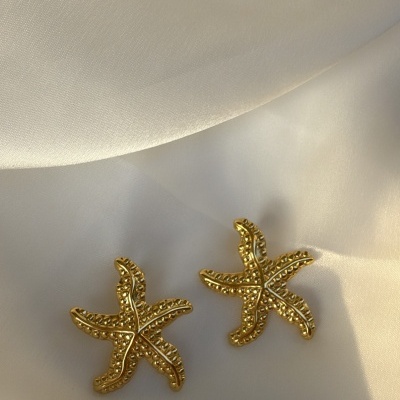 Brincos dourados em forma de estrela-do-mar sobre tecido branco