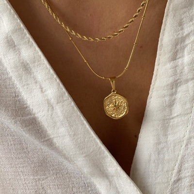 Colar duplo dourado com pendente de rosa dos ventos sobre camisa branca com botão