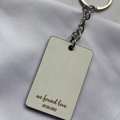 Porta-chaves metálico com pendente retangular prateado e texto gravado 'we found love 07.01.2012' sobre tecido branco