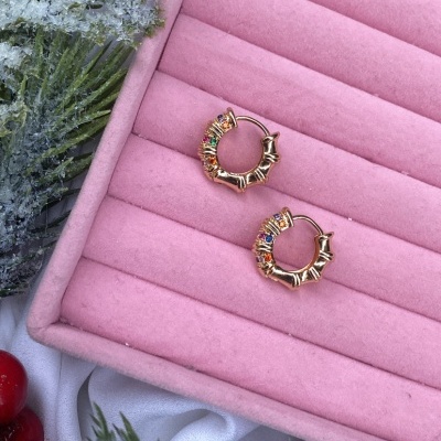 Brincos de argola dourados com pedras coloridas numa caixa rosa e decoração natalícia.