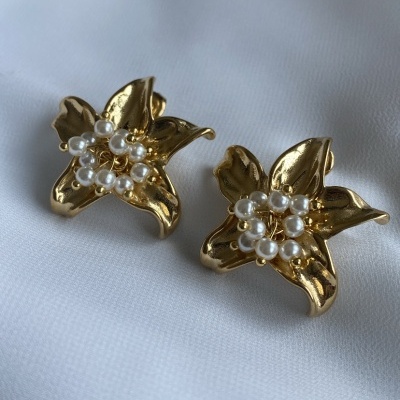 Brincos dourados em forma de flor com pérolas no centro sobre tecido branco