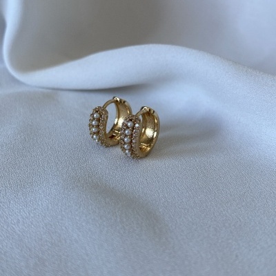 Brincos de argola dourados com pérolas sobre tecido branco