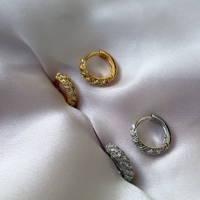 Brincos argola dourados e prateados com pedras sobre tecido branco acetinado