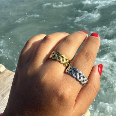 Mão com anéis dourado e prateado e pulseira rosa junto à água