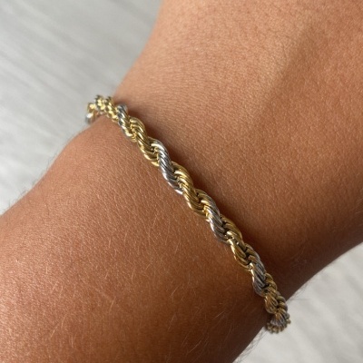 Pulseira trançada dourada e prateada num pulso com fundo cinzento claro
