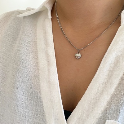Colar prateado com pendente de coração usado por pessoa com camisa branca