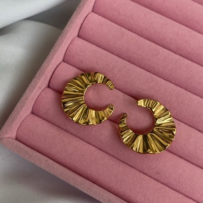 Brincos dourados com textura ondulada numa caixa rosa de veludo