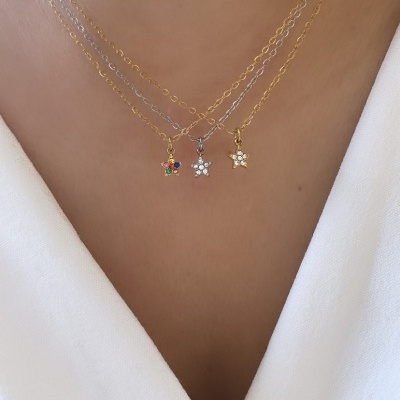 Três colares finos com pendentes em forma de flor, dois dourados e um prateado, em decote branco.