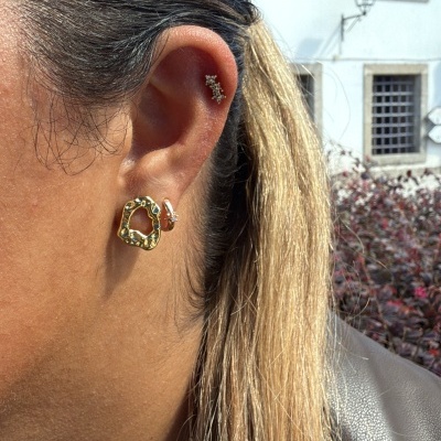 Brincos dourados com textura e pérolas em orelha feminina ao ar livre