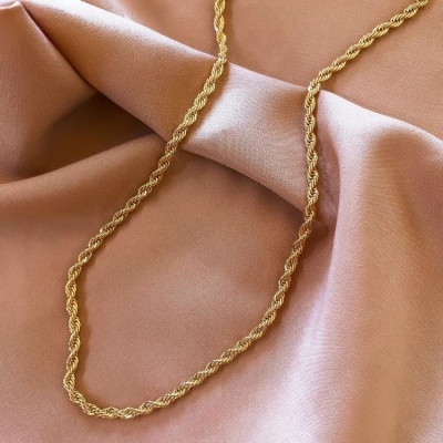Colar dourado de corrente torcida sobre tecido rosa claro acetinado