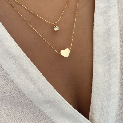 Colar duplo em ouro com pendentes de círculo e coração, camisa branca com botão castanho