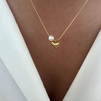 Colar dourado com coração e pérola sobre blusa branca