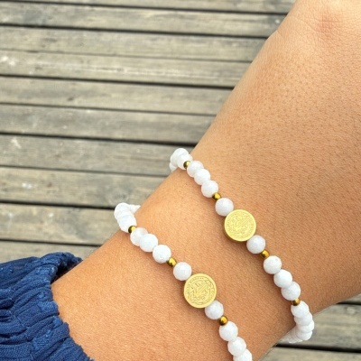 Pulseiras de contas brancas com moedas douradas no pulso