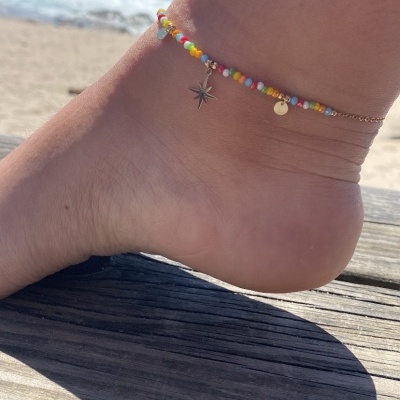 Pulseira de tornozelo colorida com pendentes metálicos na praia