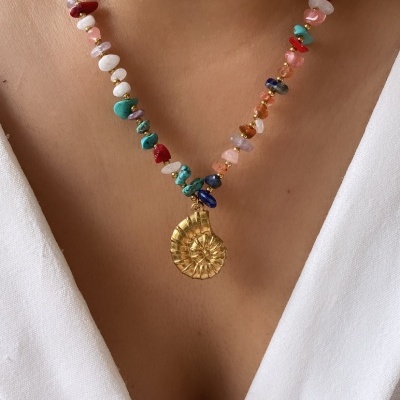 Colar com pedras coloridas e pendente dourado em forma de espiral sobre pele clara e vestido branco