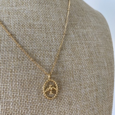 Colar dourado com pendente circular trançado e folhas numa base de tecido bege