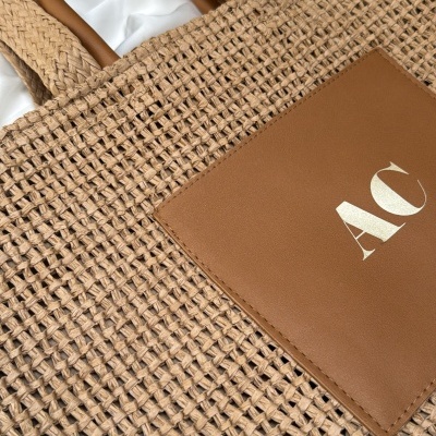 Saco de mão de tecido ráfia castanho claro com alças castanhas e bolso frontal em pele castanha com letras AC